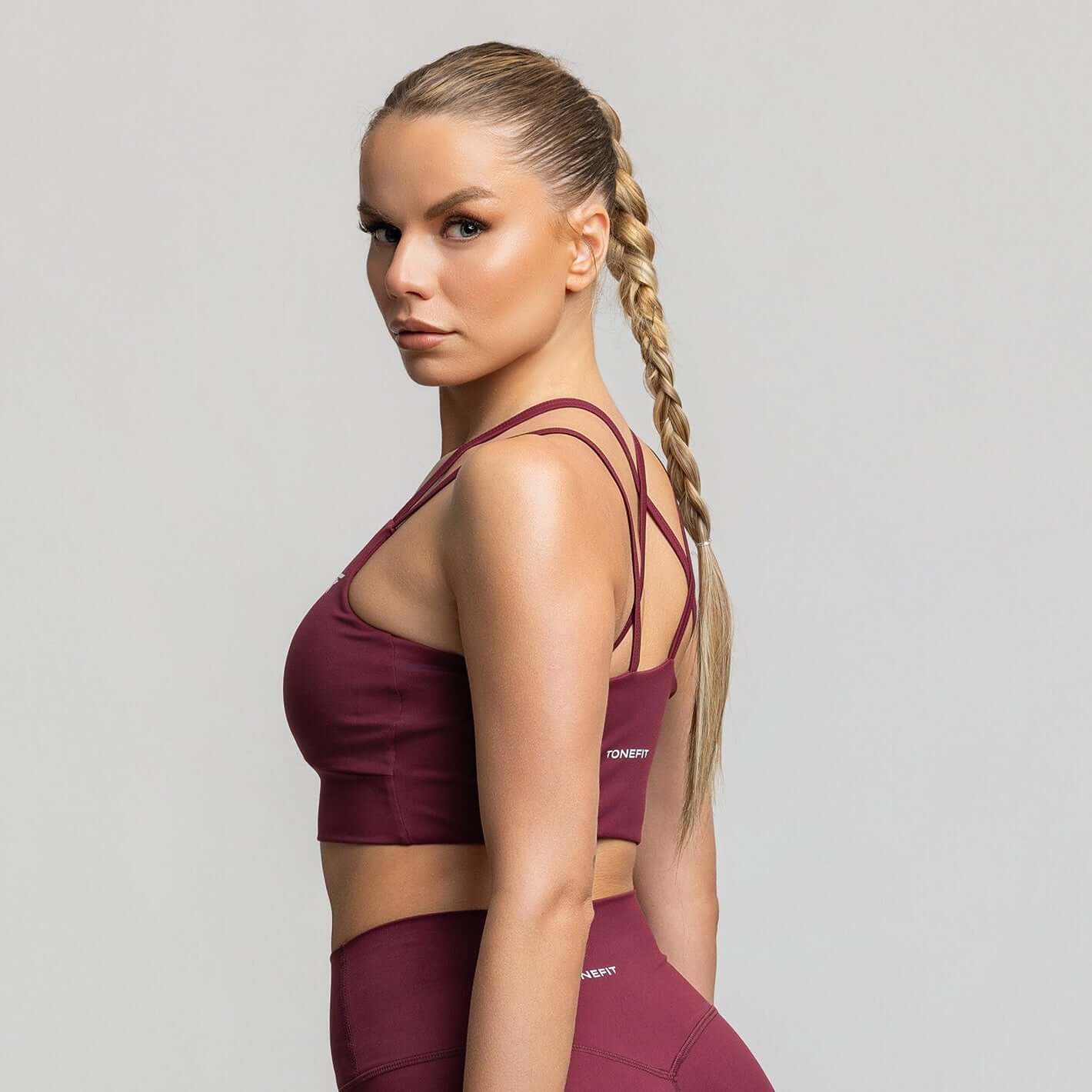 Model showcasing the Criss Cross Back Sports Bra in burgundy, perfect for dynamic workouts and stylish training.