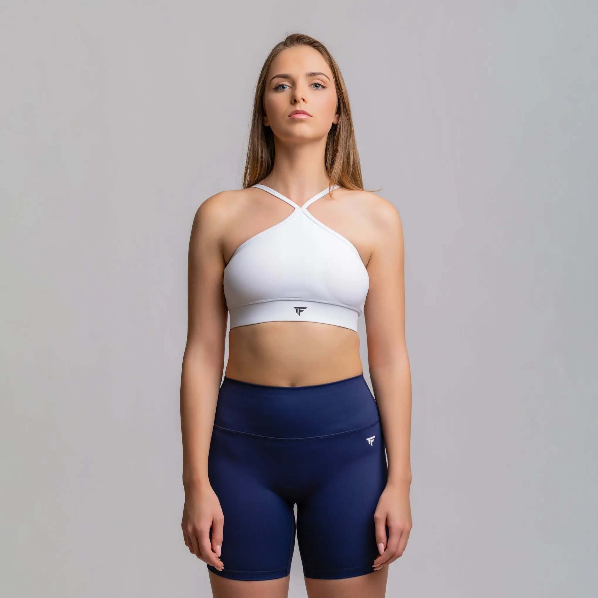 Halter neck sports bra in white with crisscross straps, paired with navy shorts for a stylish athletic look.