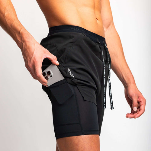 Model wearing 2-in-1 hybrid training shorts, pulling phone from pocket, showcasing functionality and style.